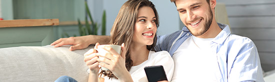 A couple sitting on the couch enjoying a coffee and looking at their phone.